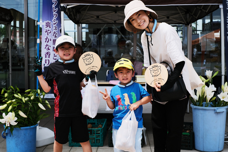 詰め放題で詰めた野菜を持って笑顔でブイサインをする親子の写真